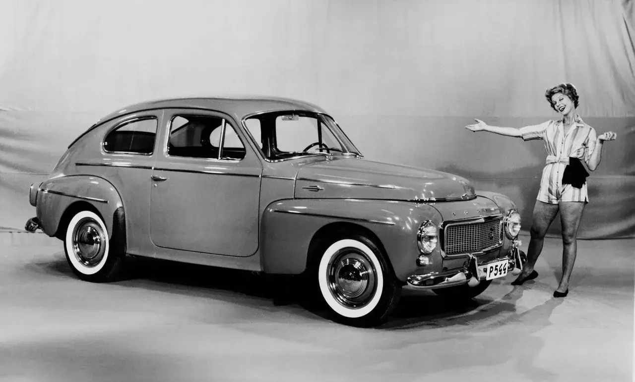 En glad kvinna poserar bredvid en klassisk Volvo PV 444.