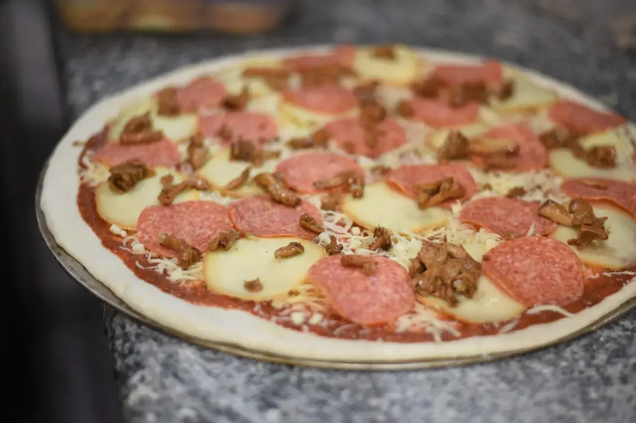 Gotowa do pieczenia pizza z salami, mozzarellą i grzybami. Idealna na kolację po włosku.