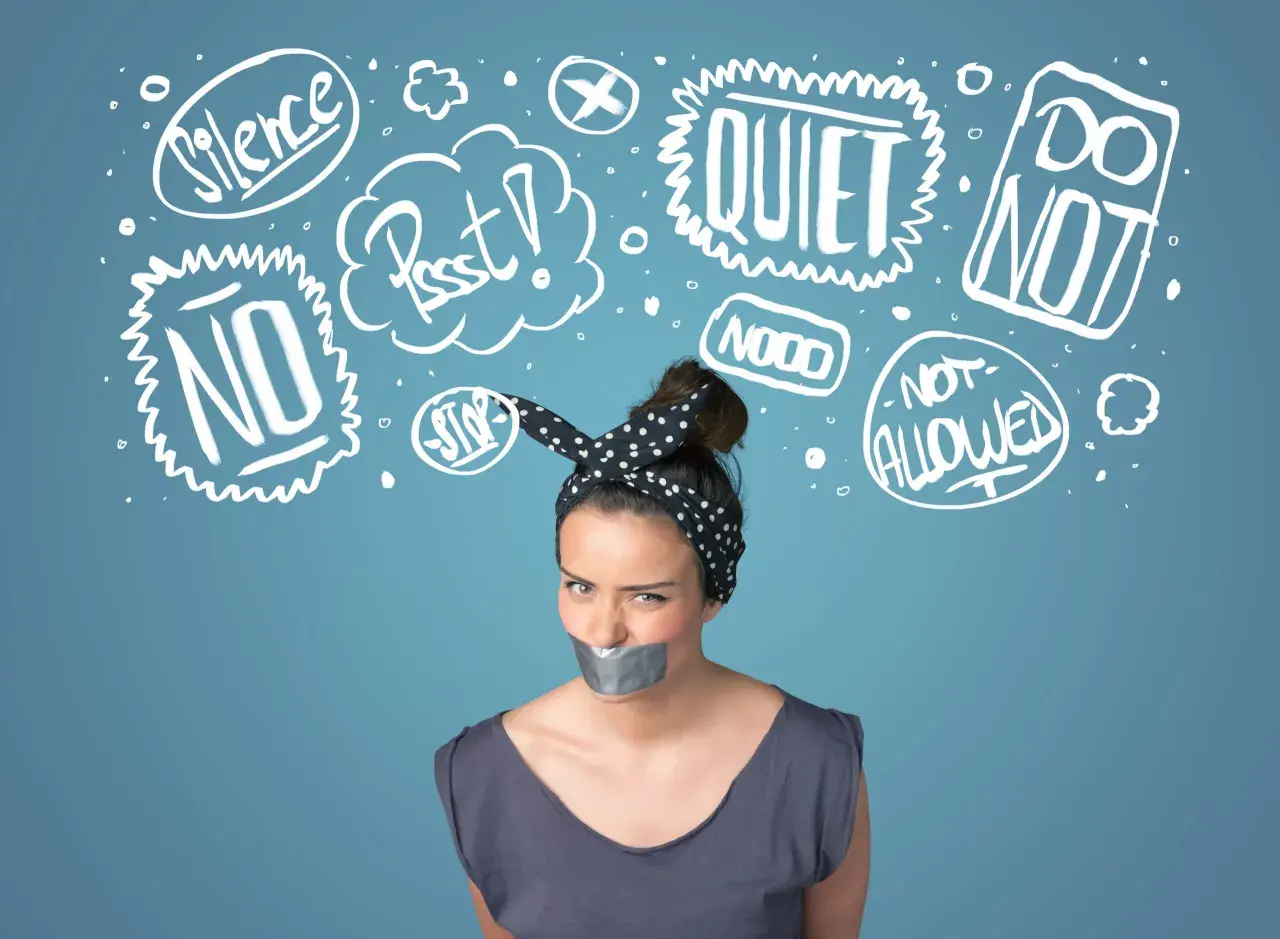 Kobieta z zaklejoną taśmą ustami, otoczona chmurkami z napisami "Silence", "Quiet", "No", "Stop", symbolizującymi tłumienie emocji.
