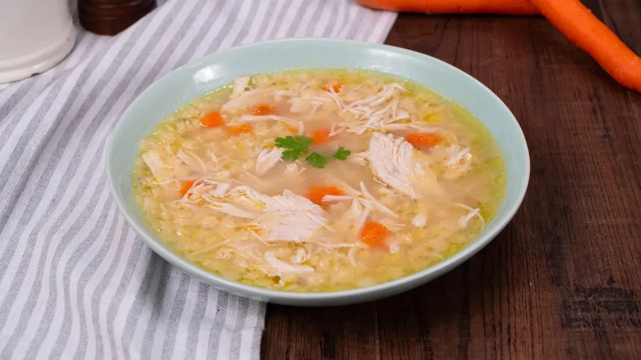 Un confortante brodo di pollo con pezzi di pollo sfilacciato, carote e un rametto di prezzemolo.