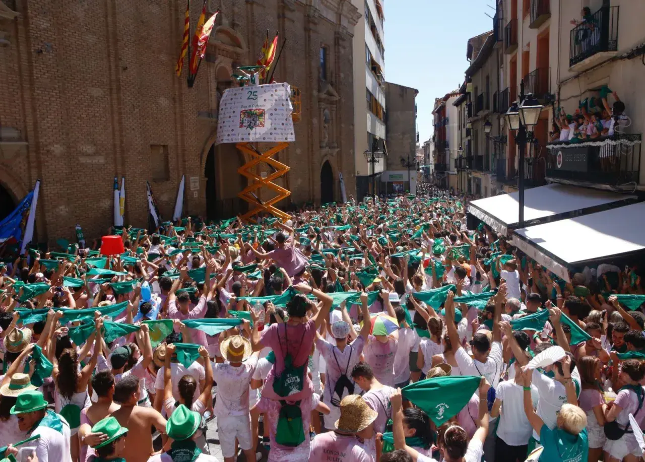 Multitud celebra el programa fiestas Huesca, agitando pañuelos verdes. Un cartel anuncia "25".