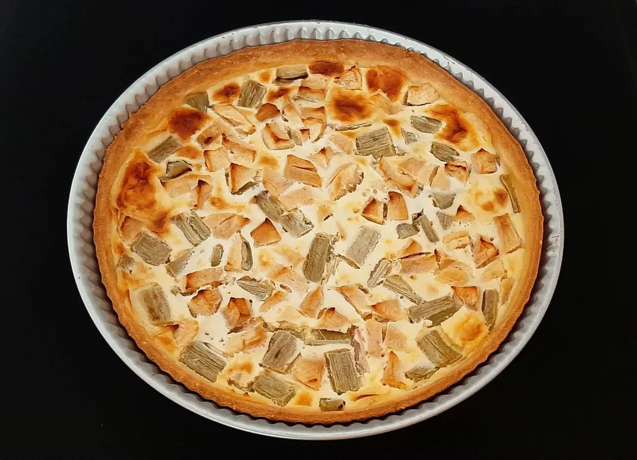 Tarte rhubarbe pomme dorée, garnie de morceaux de fruits et d'une crème onctueuse, prête à être dégustée.
