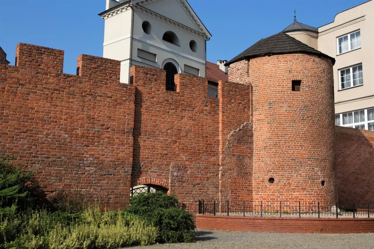 Kamienna baszta obronna, znana jako baszta Dorotka, z charakterystycznym stożkowym dachem, otoczona ceglanym murem.
