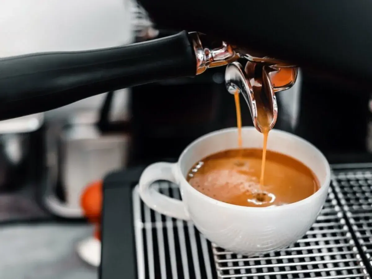 En espressomaskin hjälper till att brygga espresso. Varm, gyllene kaffe rinner ner i en vit kopp.
