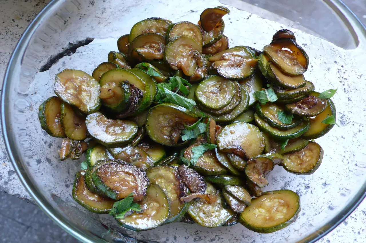 Zucchine alla scapece, fritte e condite con aceto e menta, in una ciotola di vetro.