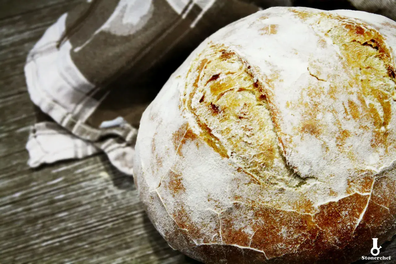 Świeżo upieczony bochenek chleba na drożdżach, oprószony mąką, leży obok lnianej ściereczki. Idealny przepis na chleb na drożdżach.