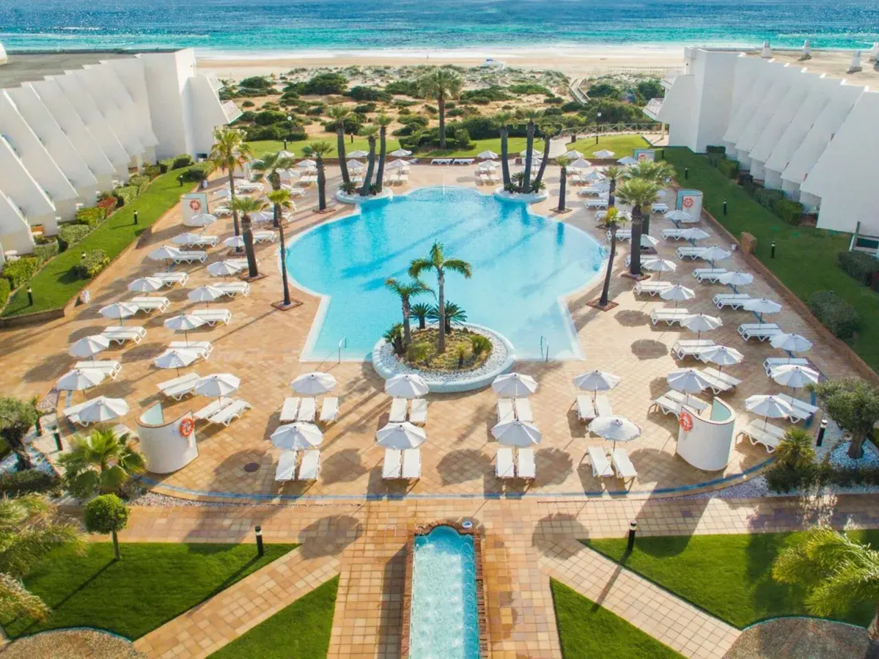Traumhafter Poolbereich mit Liegen und Sonnenschirmen am IBEROSTAR Royal Andalus. Der Strand und das Meer sind im Hintergrund zu sehen.