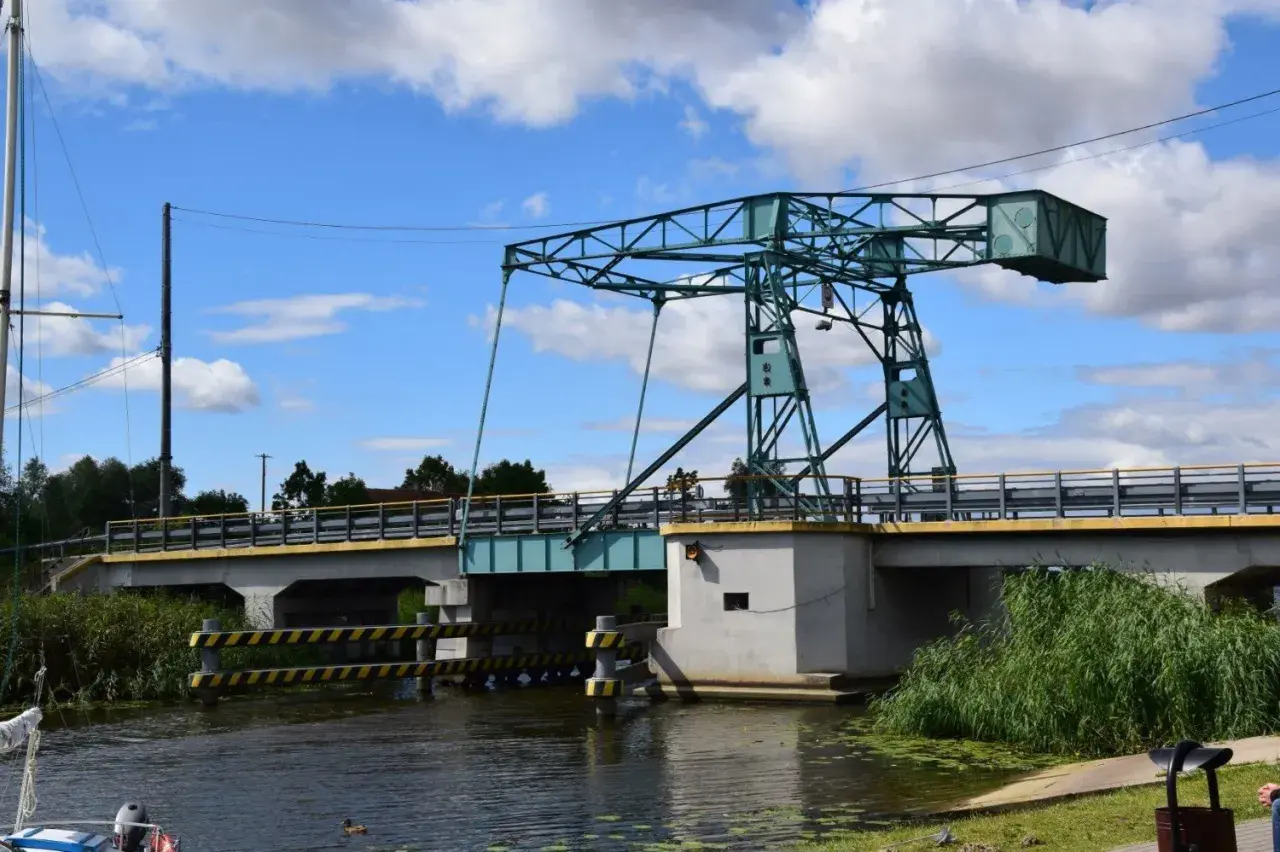 Most czterech pancernych, podnoszony most nad kanałem, z zieloną konstrukcją i błękitnym niebem.
