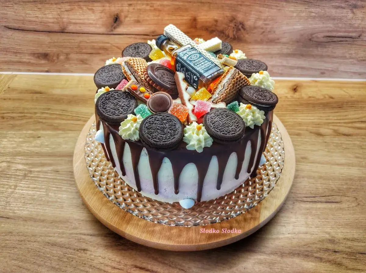 Tort z polewą czarny drip, ozdobiony ciasteczkami Oreo, waflem i mini buteleczką Jack Daniel's.