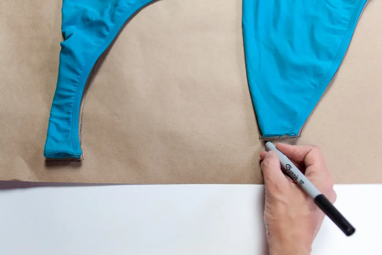 Tracing a blue swimsuit piece onto brown paper, a step in how to make a swimsuit.