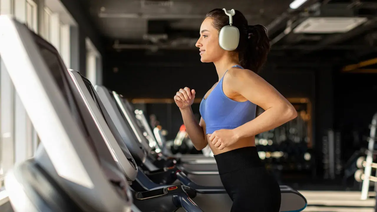 Junge Frau läuft auf Laufband im Fitnessstudio, motiviert für Fitness und Abnehmen.
