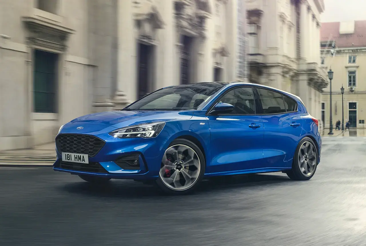 Ford Focus blu in movimento, disponibile con motori a benzina e diesel, sfreccia in una strada cittadina.