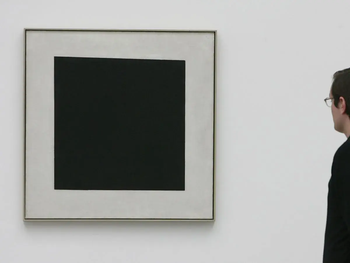 Ein Mann betrachtet ein schwarzes Quadrat auf hellem Grund. Die schlichte Komposition lässt Raum für Interpretationen, die schwarzes Quadrat Bedeutung.