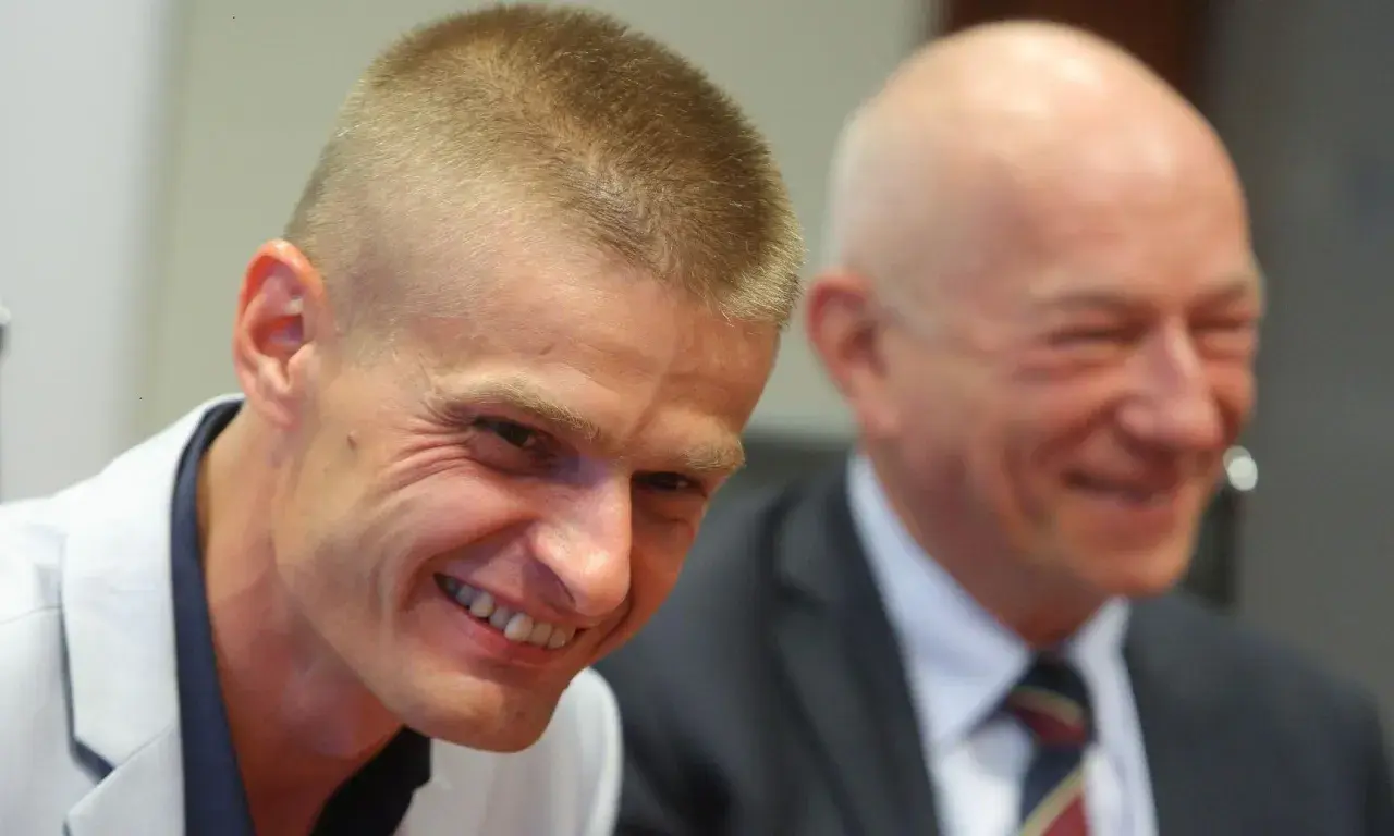 Uśmiechnięty Tomasz Komenda, który otrzymał ogromne odszkodowanie za niesłuszne skazanie, siedzi obok drugiego mężczyzny.