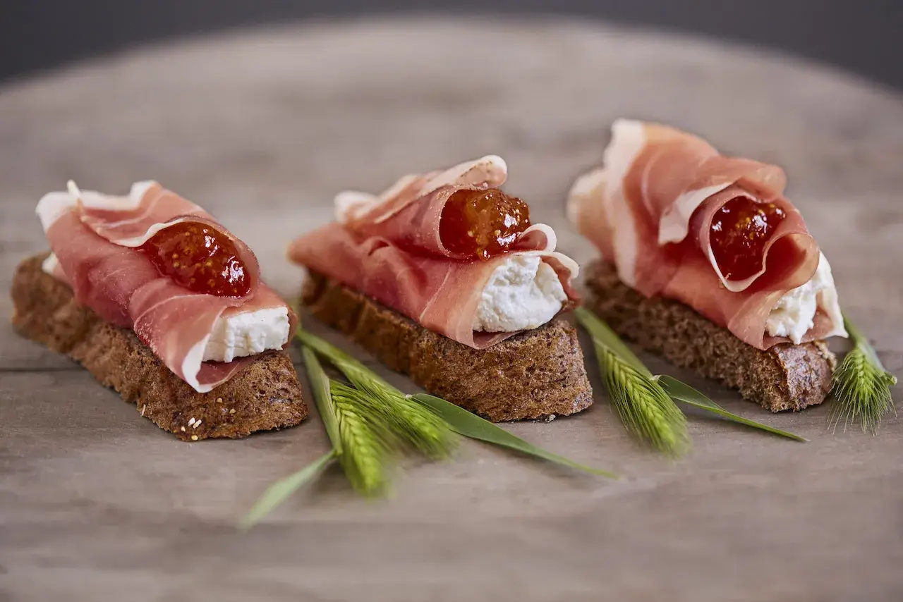 Drei kleine Brote mit Frischkäse, Feigenmarmelade und Schinken – so sieht ein köstliches Crudo aus.