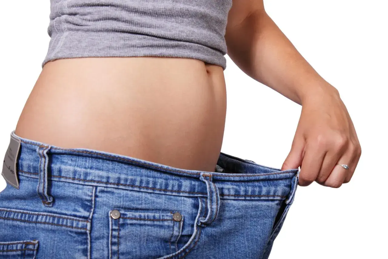 En kvinna håller upp sina jeans som är för stora, ett tecken på att hon lyckats gå ner i vikt efter graviditet.