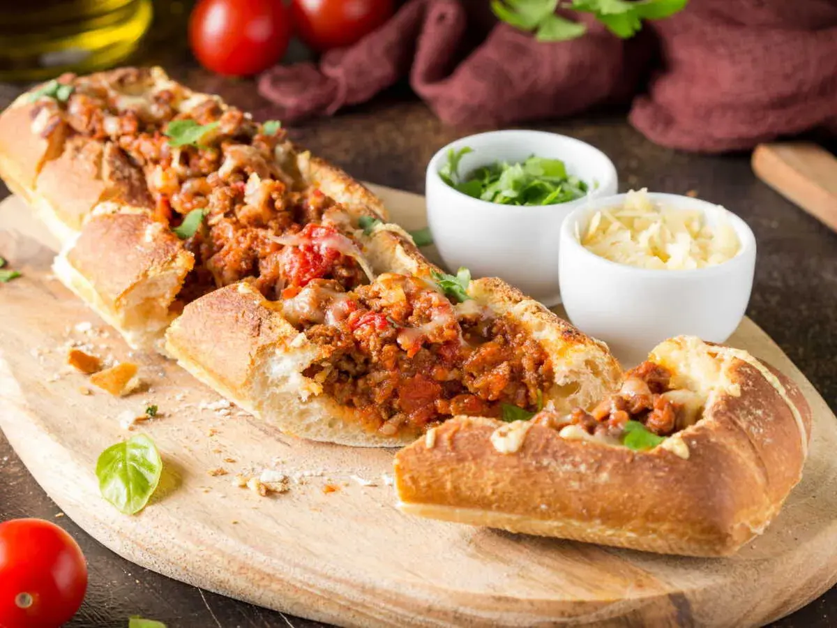 Une baguette farcie généreusement avec une sauce à la viande savoureuse et du fromage fondant, prête à être dégustée.