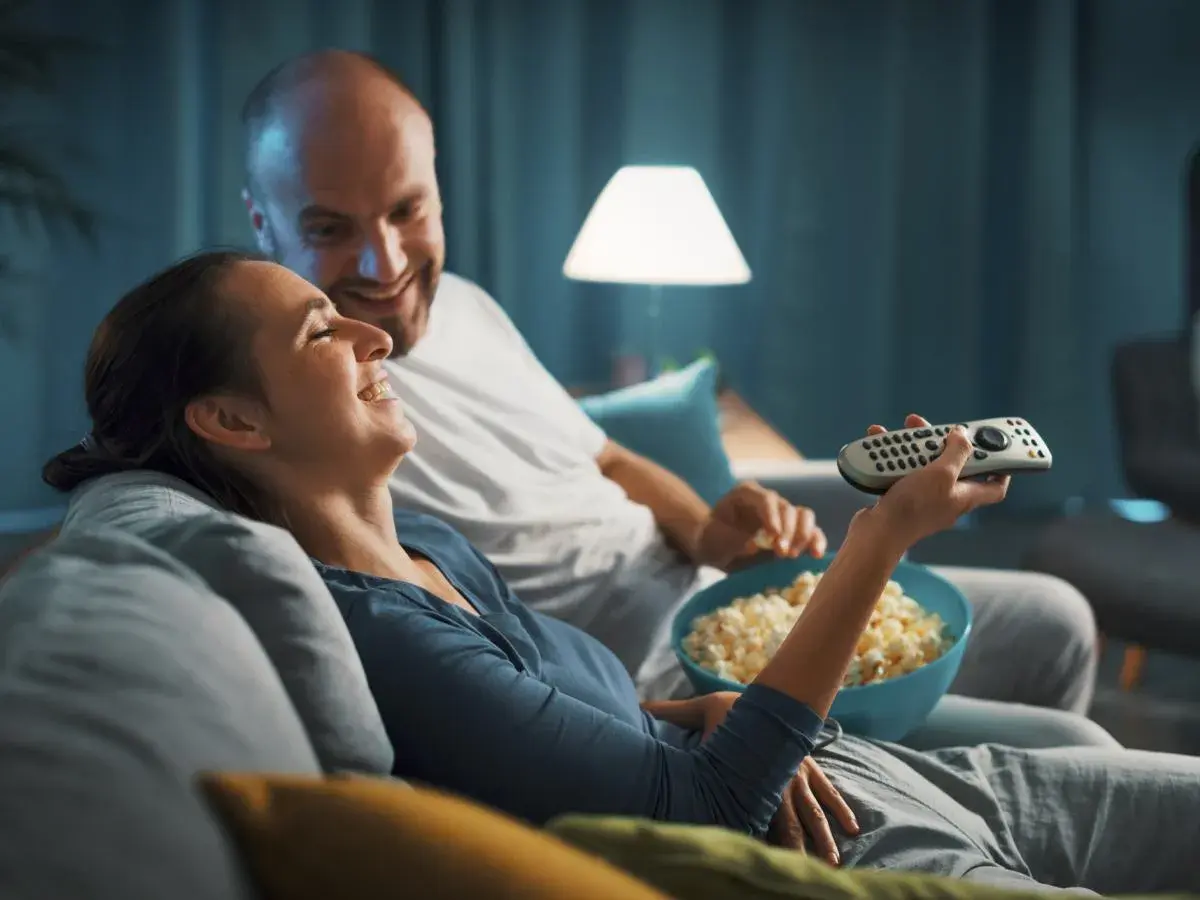 Para spędza miły wieczór, śmiejąc się i jedząc popcorn. Idealny czas na fajne filmy romantyczne na wieczór.