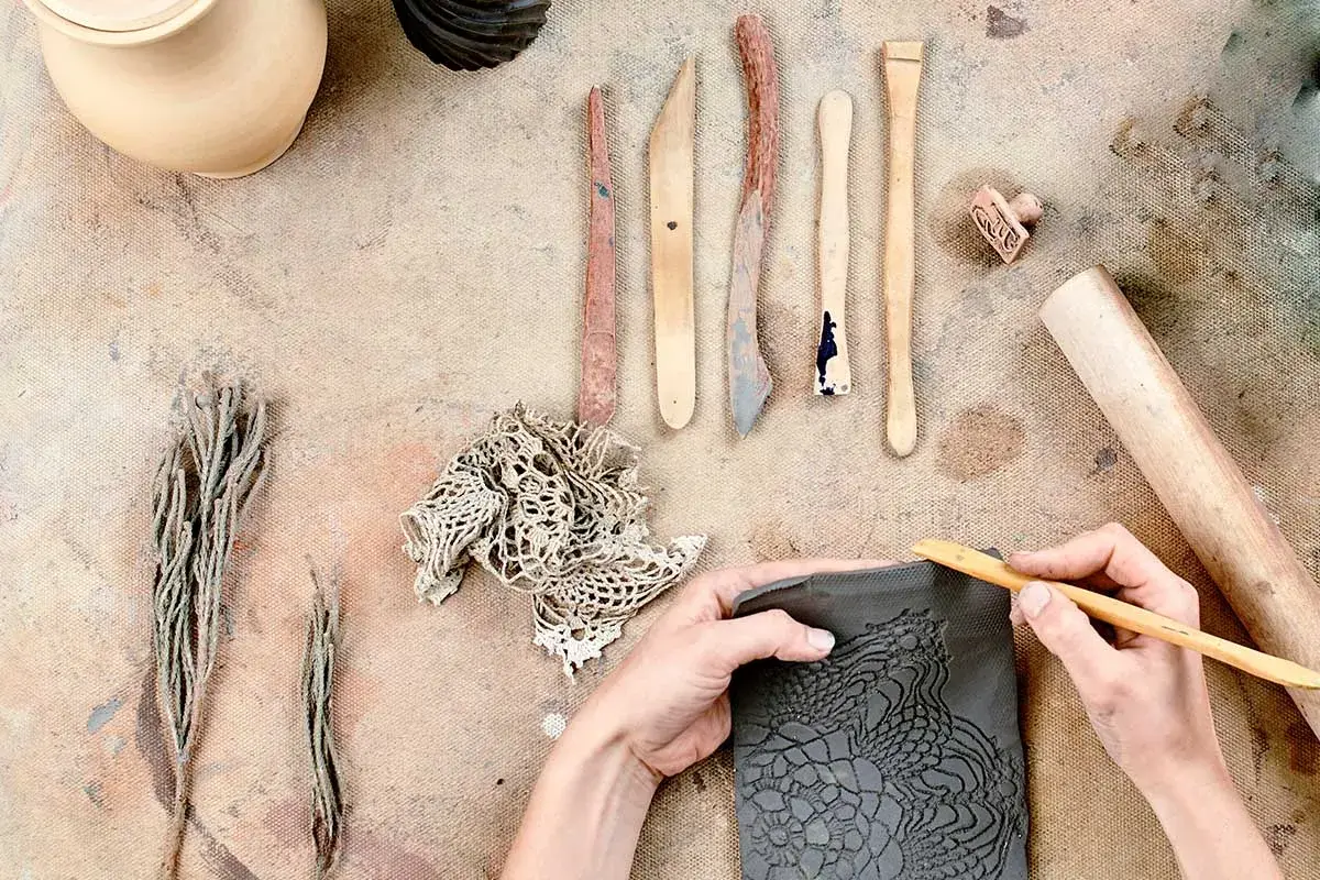 Mani che lavorano con il das adulti, creando un motivo a pizzo su argilla con strumenti da scultore.