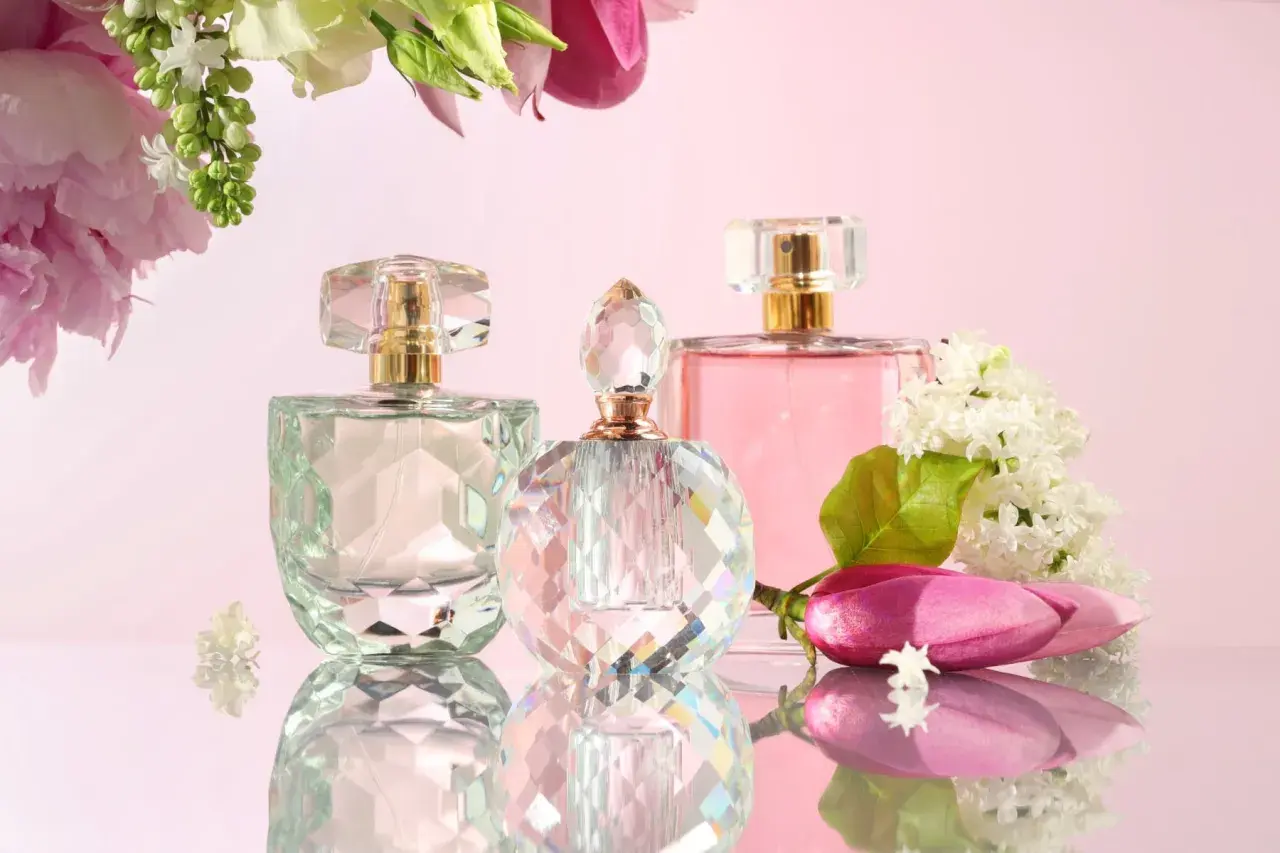 Eleganckie flakoniki perfum, w tym jeden z zielonkawym szkłem, otoczone kwiatami. To idealny prezent, gdy szukasz tłumaczenia "eau de parfum".