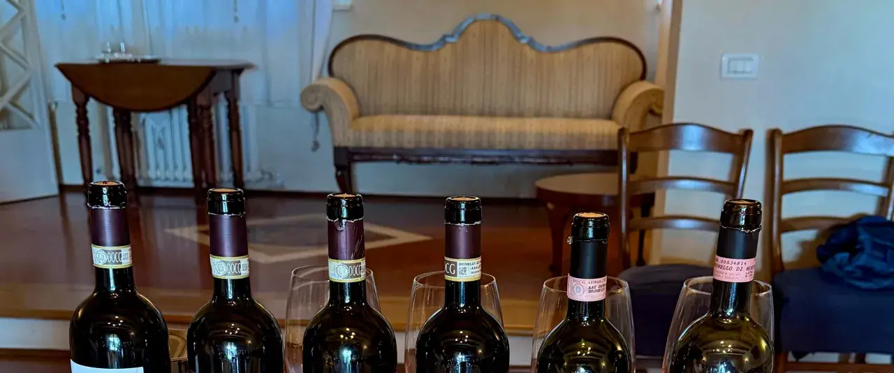 Sei bottiglie di vino, tra cui un **migliore Brunello di Montalcino**, pronte per una degustazione in un salotto elegante.