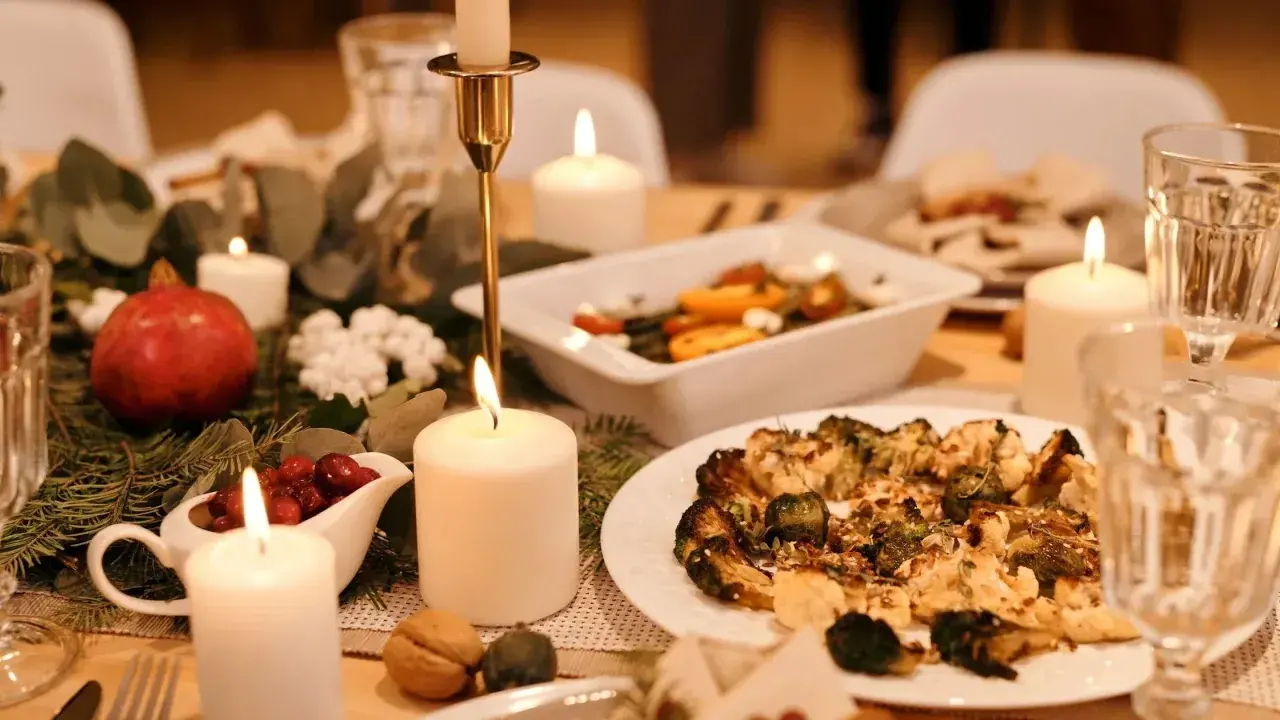 Festlich gedeckter Tisch mit Kerzenlicht, Granatapfel, Cranberry-Sauce und einem Teller mit geröstetem Gemüse – ein gesundes Weihnachtsessen.