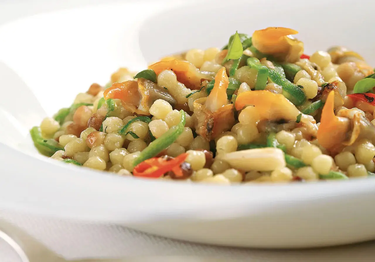 Un piatto di fregola sarda con vongole, peperoncino e zucchine, un sapore di mare e terra.