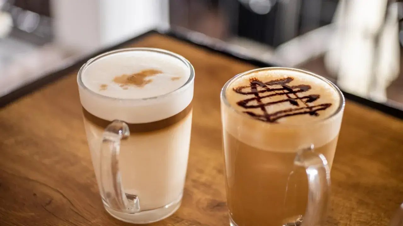 Dwie pyszne kawy latte, jedna z czekoladowym wzorem, druga z pianką i cynamonem. Idealne na chwilę relaksu.
