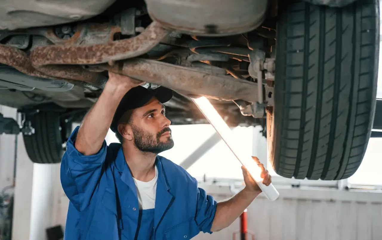 Mechanik z latarką bada podwozie auta. Upewnia się, że nie ma **braku przeglądu powyżej 30 dni**, by zapewnić bezpieczeństwo.