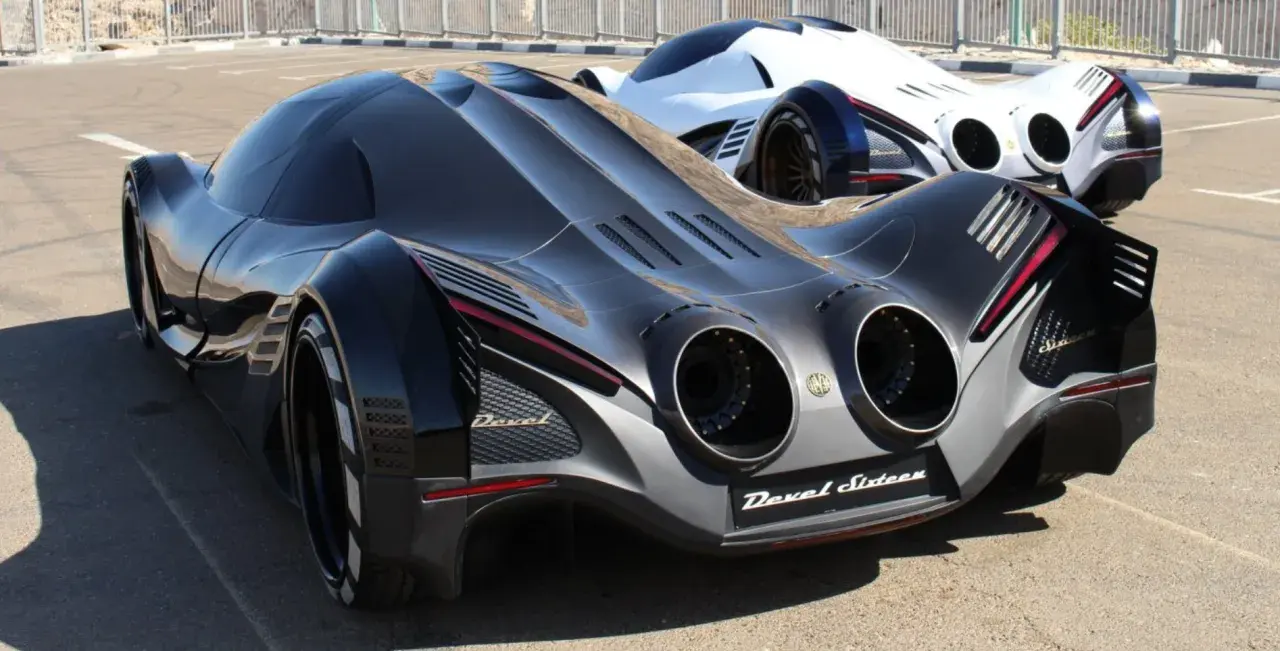 Dwa futurystyczne samochody Devel Sixteen, jeden czarny, drugi biały, stoją na asfalcie.