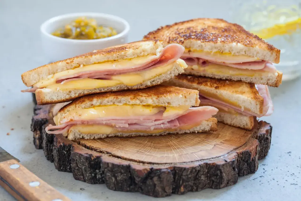 Pile de croque monsieur dorés, garniture généreuse de jambon et fromage fondant, servis sur une tranche de bois rustique.