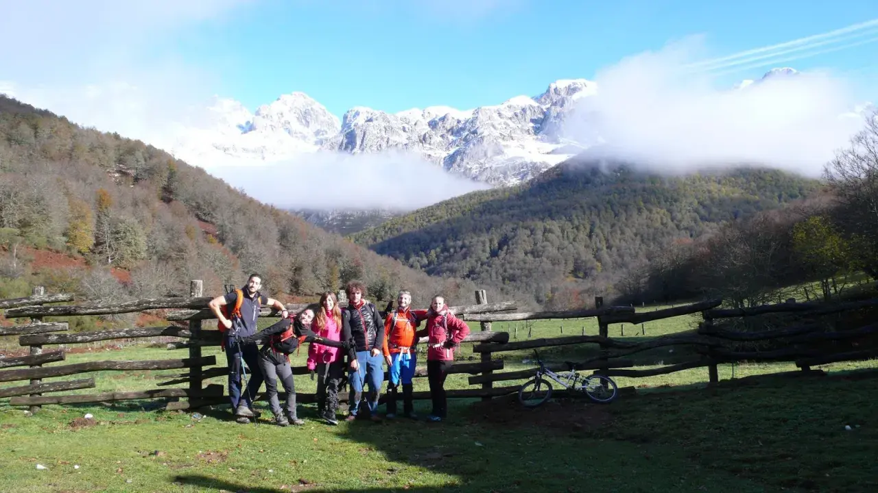 Grupo de senderistas posa junto a un cercado de madera en la ruta Soto de Sajambre-Vegabaño, con montañas nevadas al fondo.