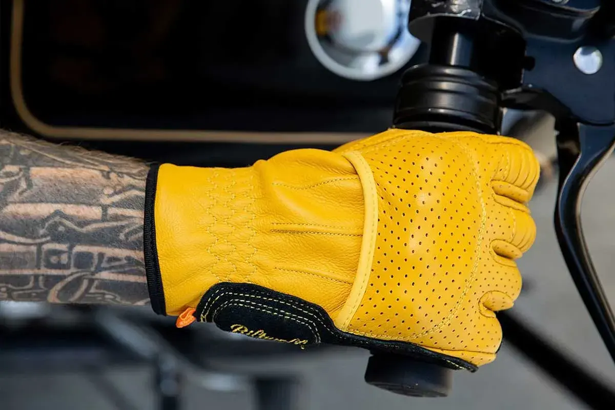 Mano tatuata con guanti Biltwell gialli traforati, pronti per un giro in moto.