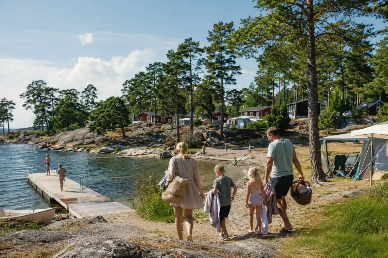 Familj på väg mot vattnet för en härlig semester med bebis i Sverige. Barnen springer glatt mot bryggan där andra badar.