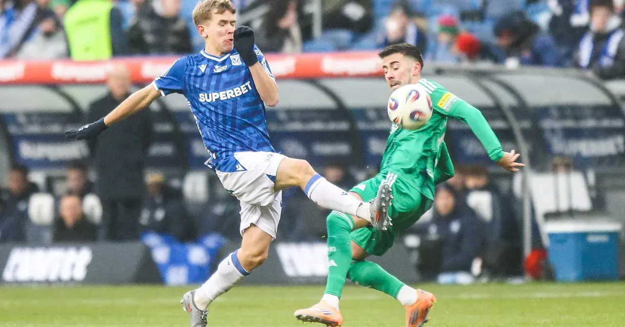 Dwóch piłkarzy walczy o piłkę. Jeden w niebieskiej koszulce, wychowanek Lecha Poznań, próbuje odebrać futbolówkę przeciwnikowi w zielonym stroju.