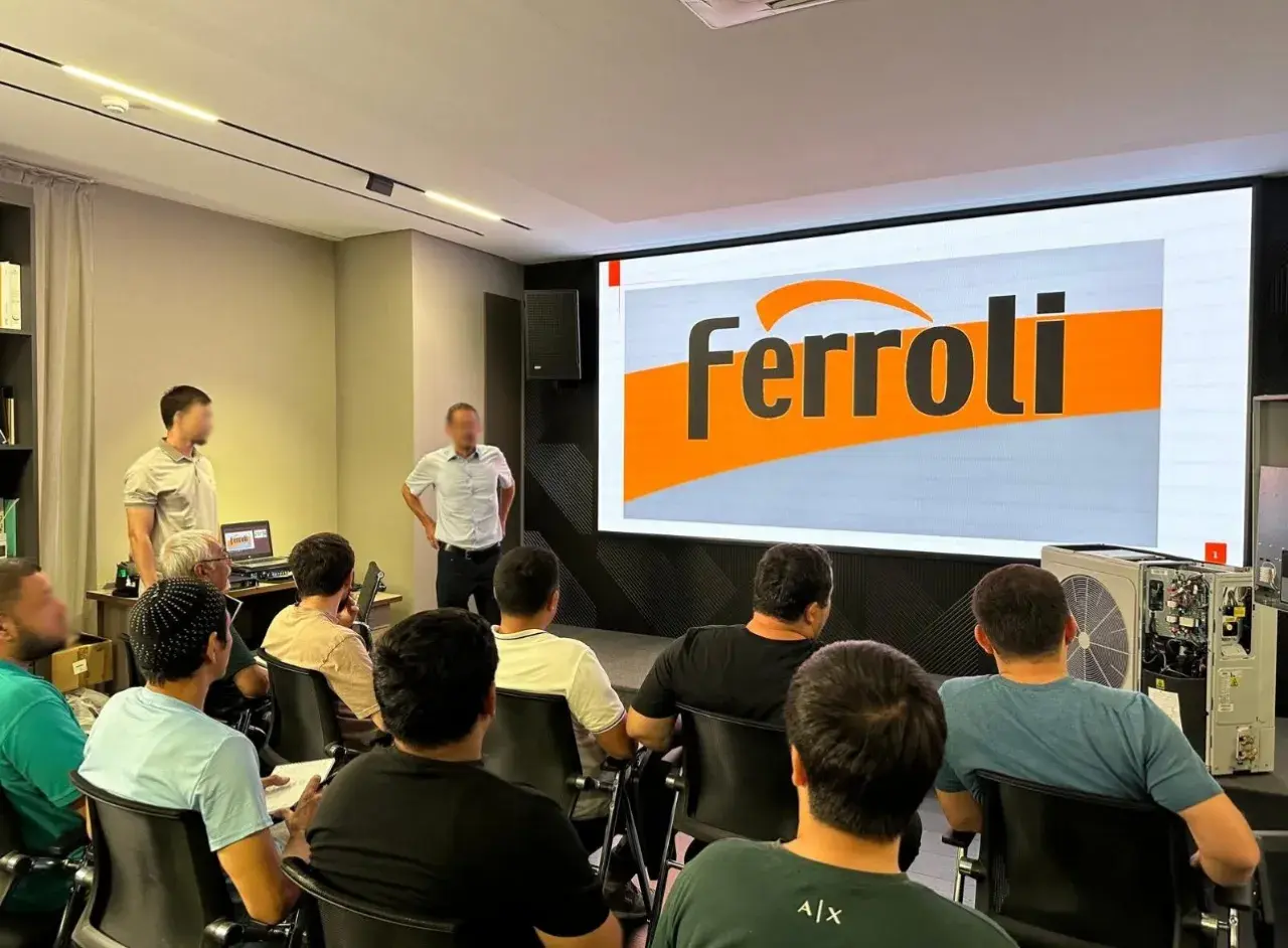 Szkolenie z serwisu Ferroli. Grupa osób słucha prezentacji na tle logo Ferroli. Kontakt do serwisu jest kluczowy.