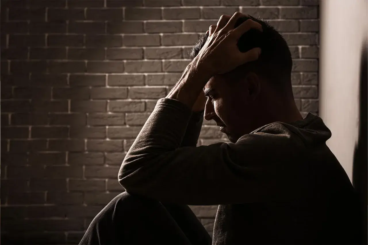 Uomo seduto con le mani tra i capelli, illuminato da un raggio di luce. Potrebbe cercare sollievo con stabilizzatori dell'umore naturali.