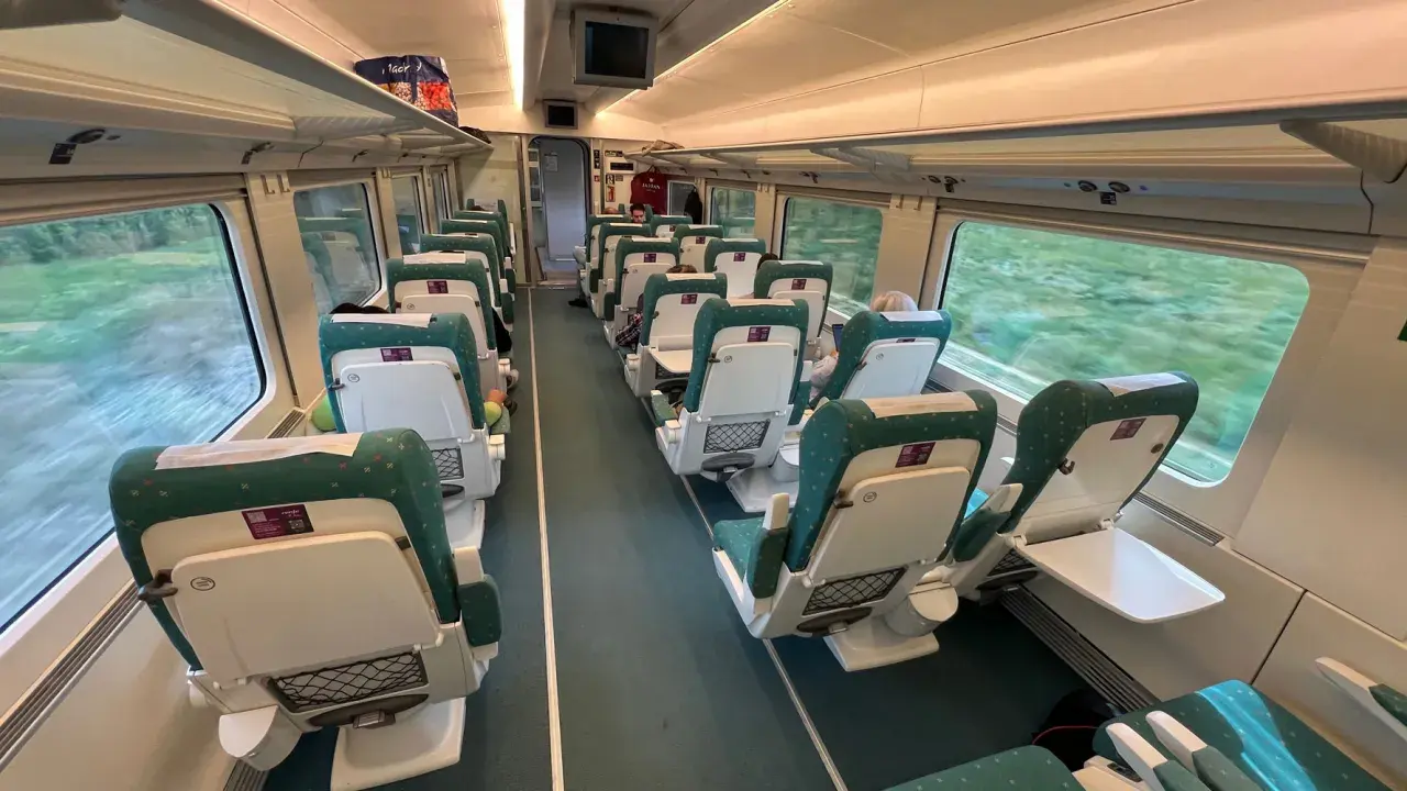 Innenraum eines Renfe Alvia Zuges mit grünen und weißen Sitzen, die auf einer Fahrt durch grüne Landschaften vorbeiziehen.