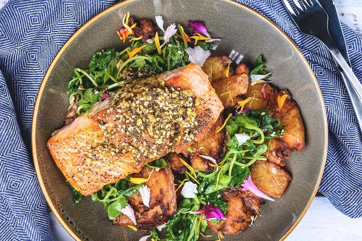 Filet de saumon croustillant, parsemé de graines, servi avec des pommes de terre rôties et une salade verte. Un accompagnement poisson savoureux et coloré.