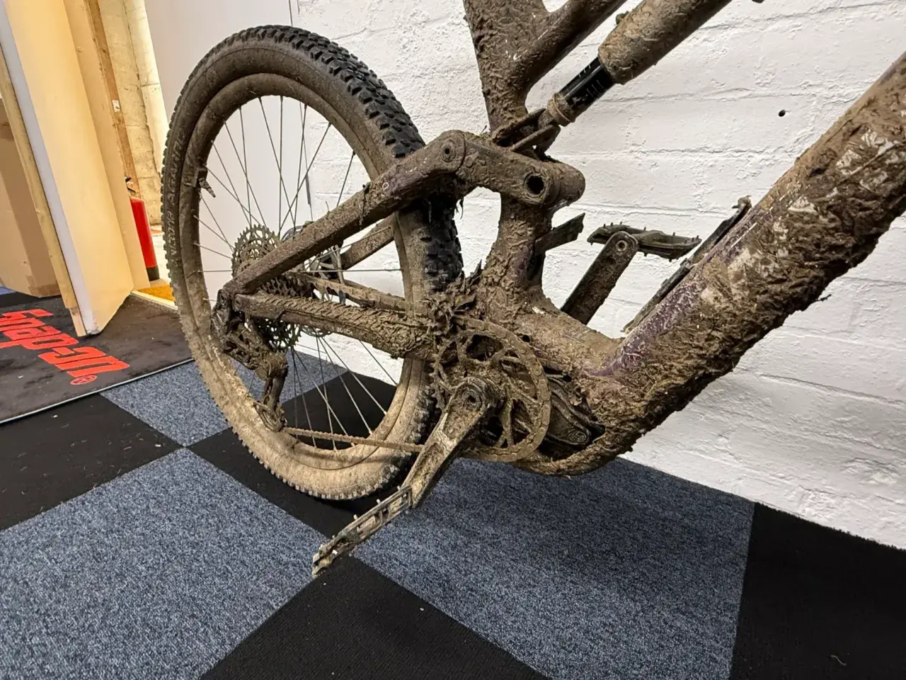 Mud-caked mountain bike rear triangle and wheel. This looks like it will be an expensive bike service cost.