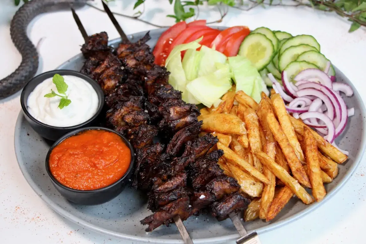 En tallrik med vegetarisk kebab på spett, serverad med pommes frites, sallad, tomat, gurka, rödlök, vit sås och en röd sås.