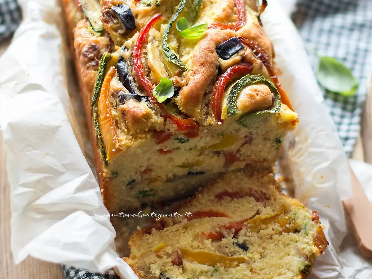 Plumcake salato ricco di verdure colorate come zucchine, peperoni e olive, guarnito con basilico fresco.