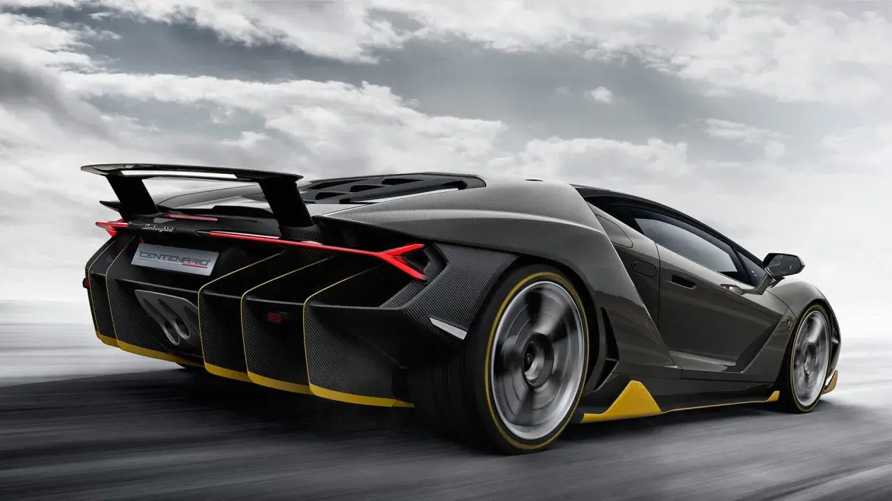 Czarny Lamborghini Centenario z żółtymi akcentami pędzi po drodze, chmury na niebie podkreślają dynamikę.