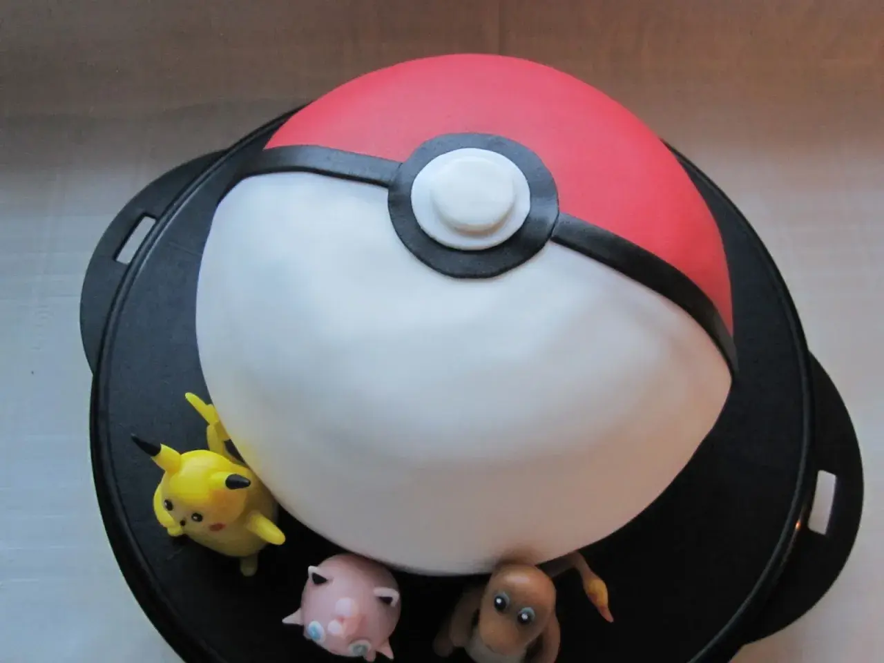 En pokemon tårta formad som en pokéboll med Pikachu, Jigglypuff och Charmander.