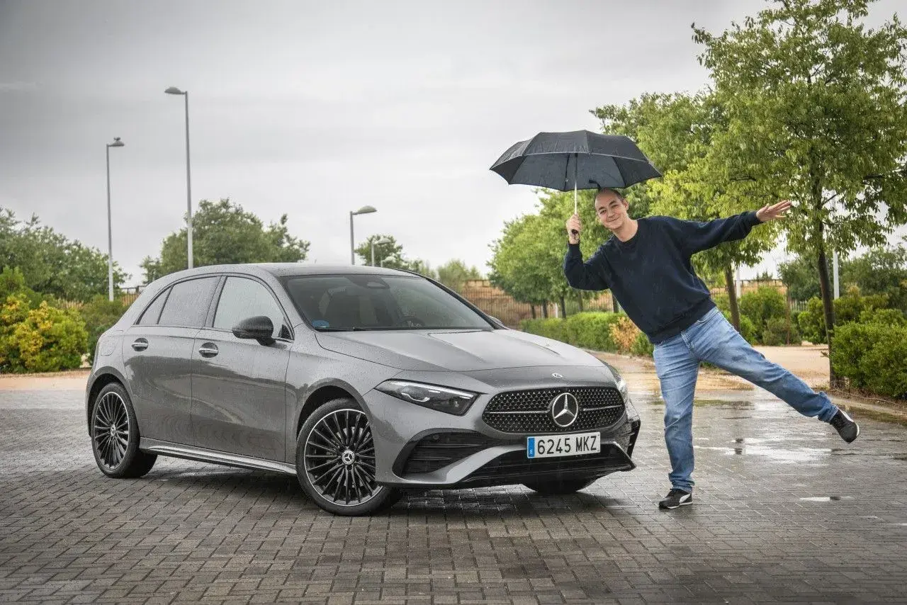 Hombre con paraguas posa junto a un Mercedes Clase A gris. ¡Una prueba de conducción bajo la lluvia!