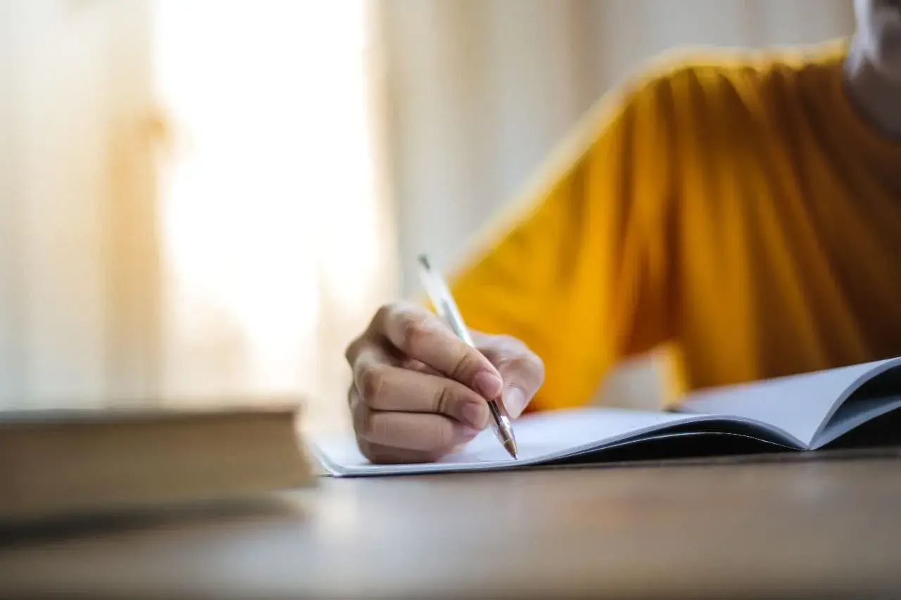 Main d'une personne écrivant dans un cahier, peut-être pour l'archive des noms de famille algériens.