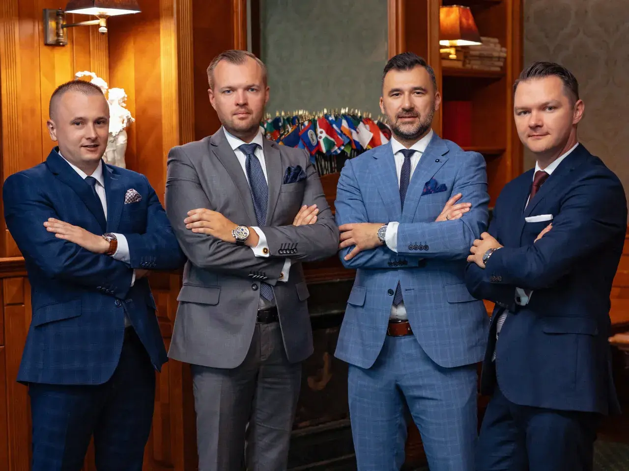 Czterech mężczyzn w garniturach stoi z rękami skrzyżowanymi na piersi.
