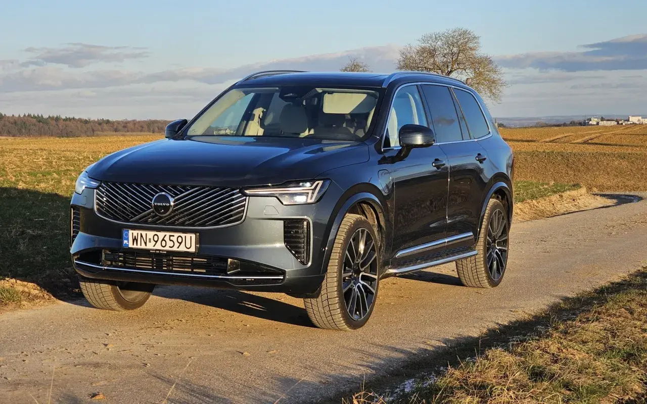 Ciemnoszary Volvo XC90 T8 na drodze polnej, z polami i drzewami w tle.