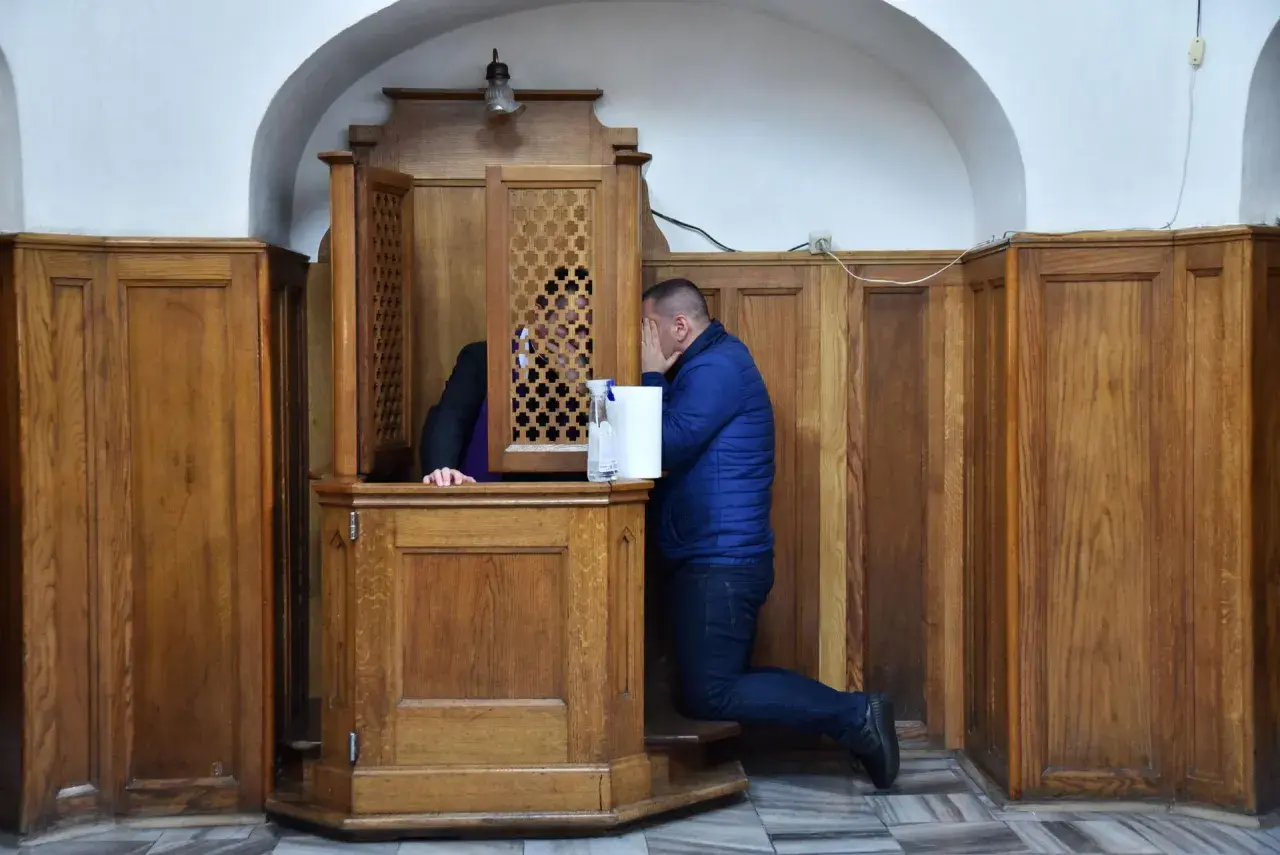 Mężczyzna klęczy przy konfesjonale, zasłaniając twarz. Czy w kościele anglikańskim jest spowiedź?