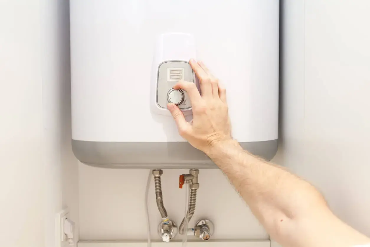 Mano ajustando el control de temperatura de un termo eléctrico.